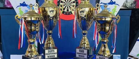 A table with three trophies labeled "Darts Championship Winner," "Darts Championship Runner Up," and "Darts Championship 3rd Place."
