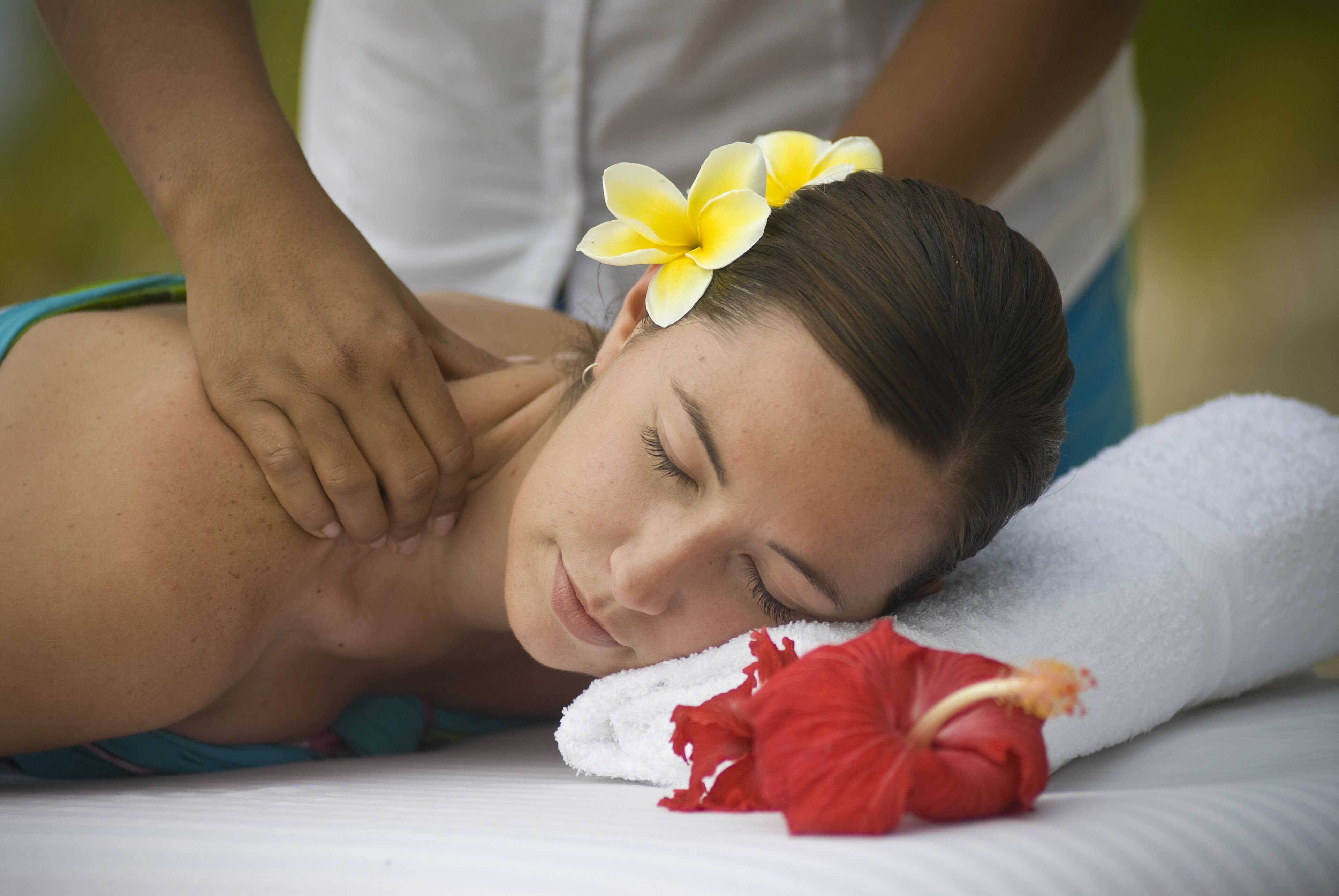 A person receiving a massage with a towel and a red flower on a massage table.