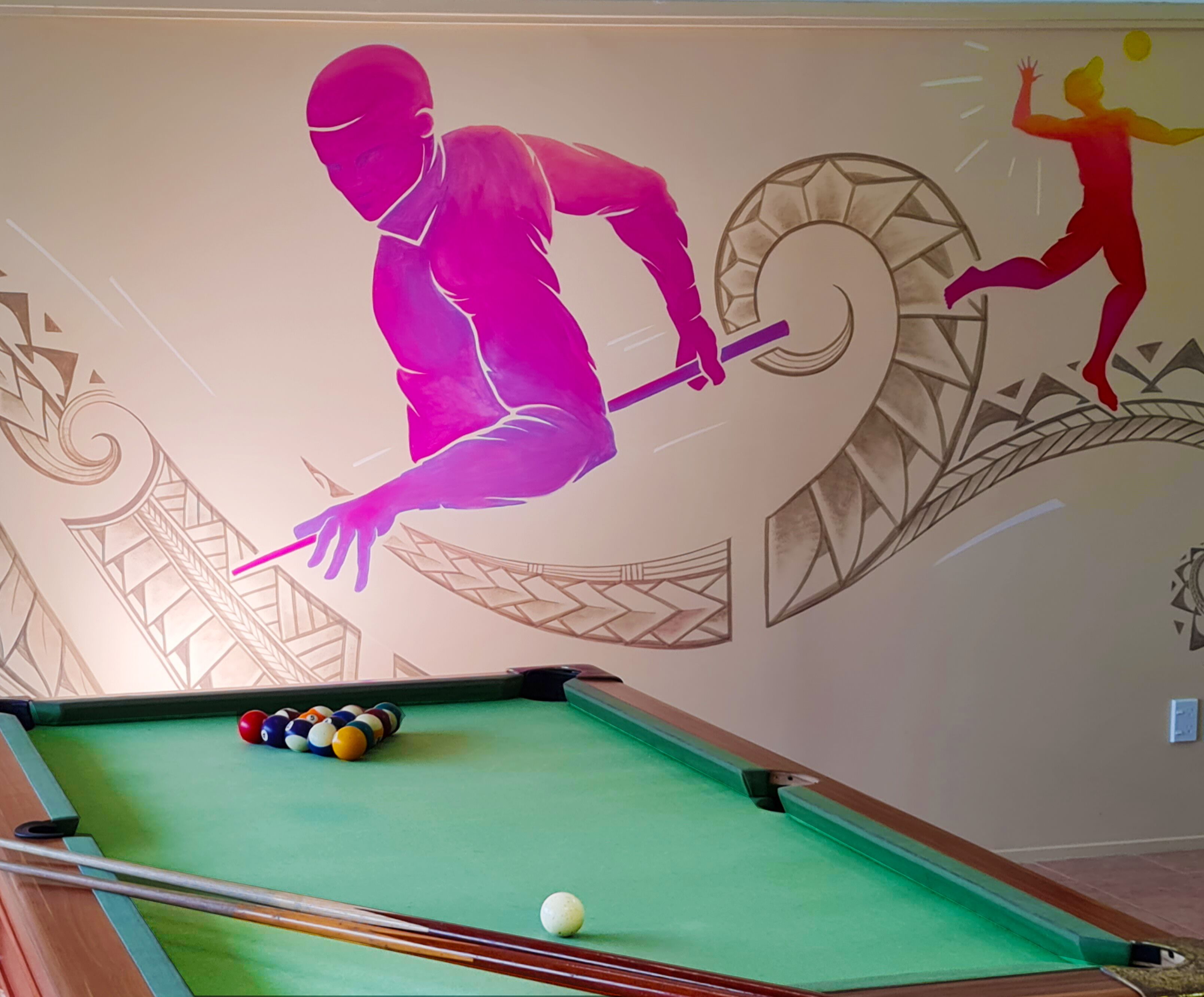 A pool table with balls and a cue stick, a wall with a mural of a person playing pool, and a decorative wall design.