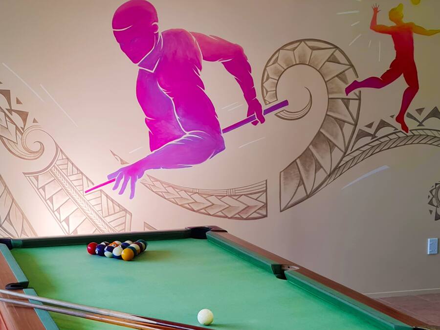 A pool table with balls and a cue stick, a wall with a mural of a person playing pool, and a decorative wall design.