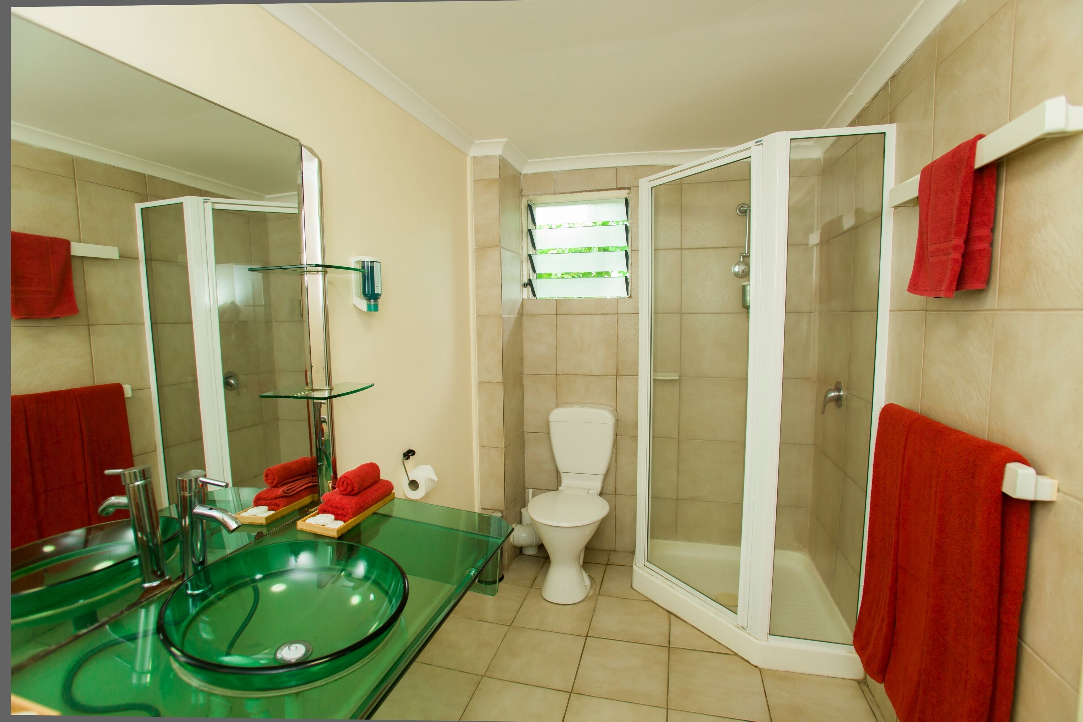 A bathroom with a glass sink, a toilet, and a glass-enclosed shower.