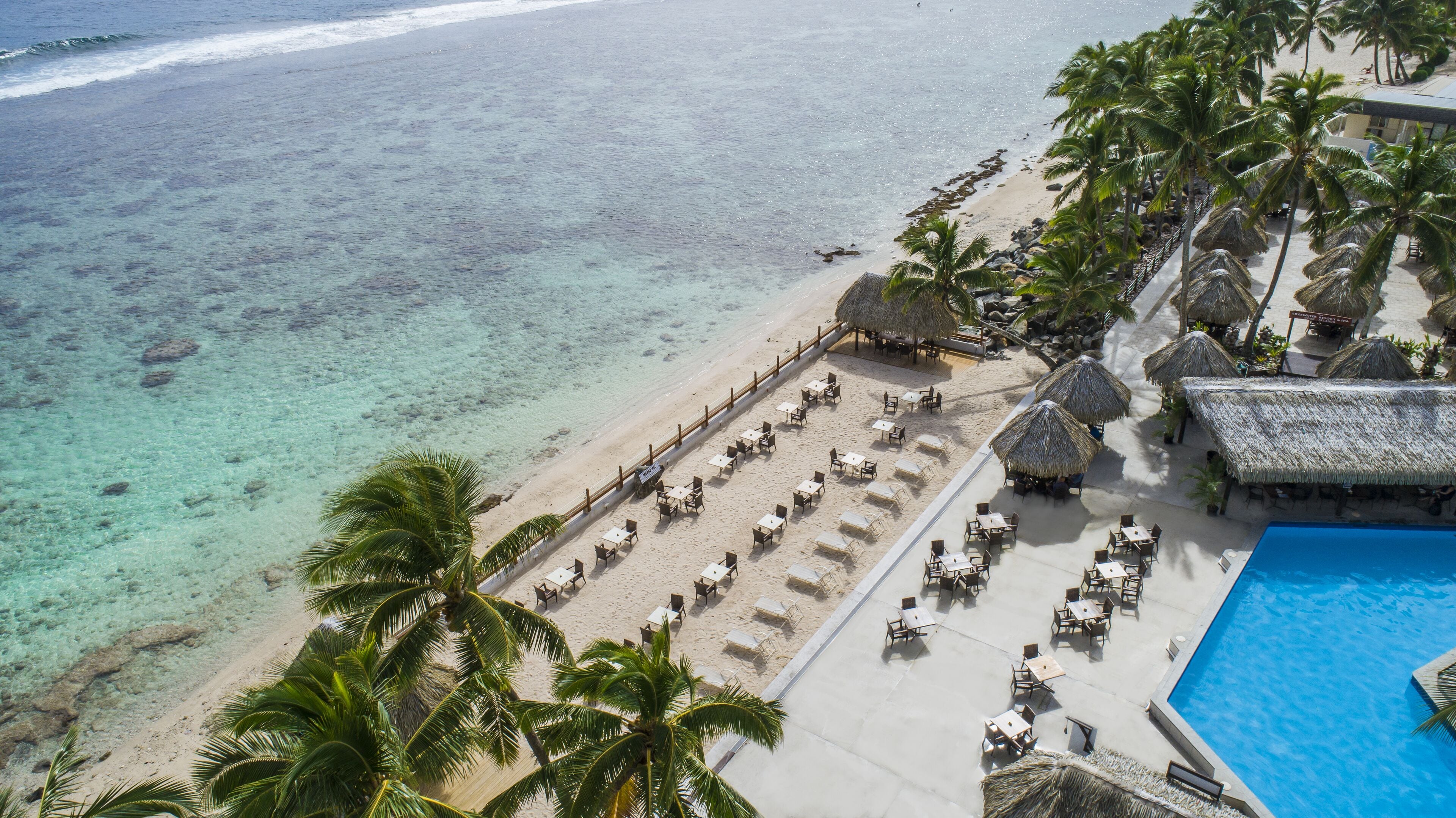 A beachside resort with a pool, lounge chairs, and palm trees.