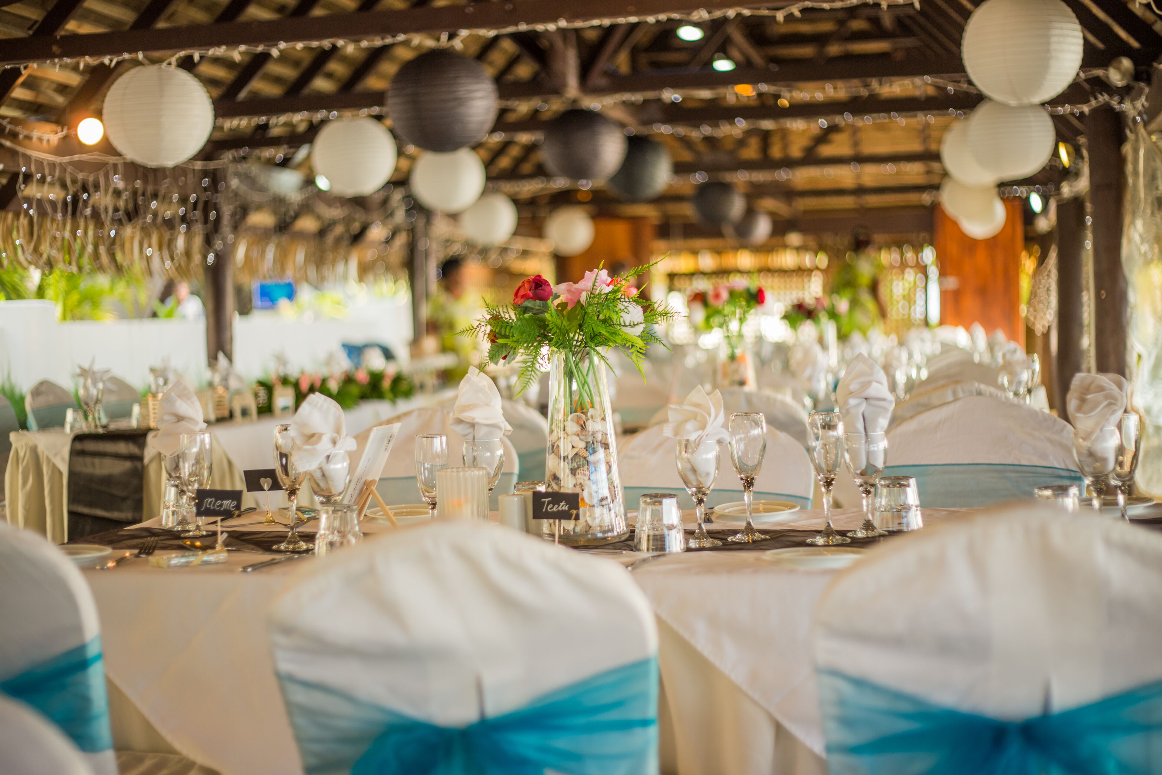 En festlokal med runda bord uppdukat för ett formellt evenemang, komplett med glasvaror, servetter och blomsterarrangemang som bordsdekoration.