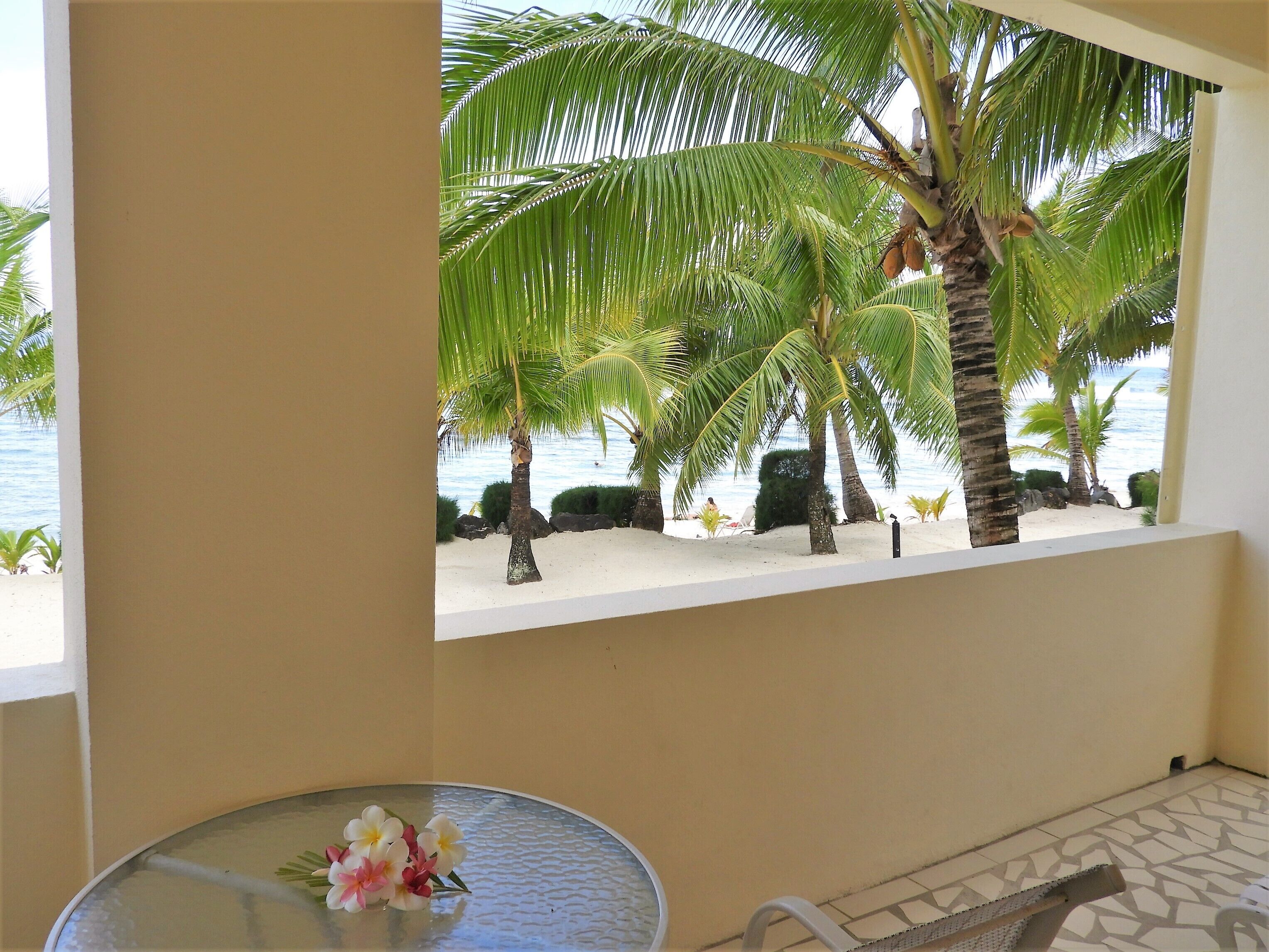 Ein Zimmer mit Blick auf einen Strand, Palmen und einen Tisch mit Blumen.
