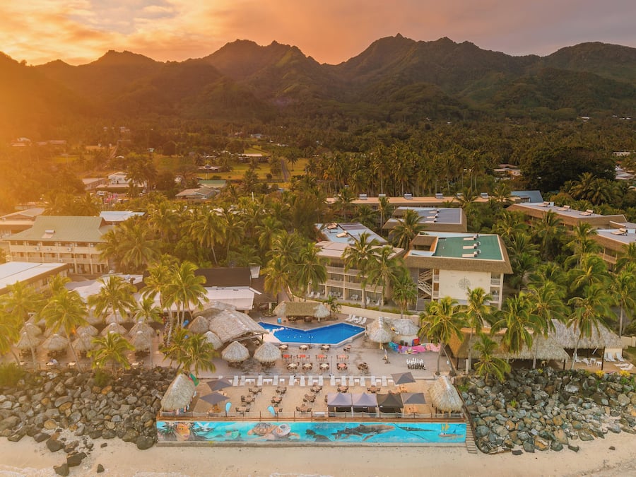 A resort with a pool, palm trees, and mountains in the background.
