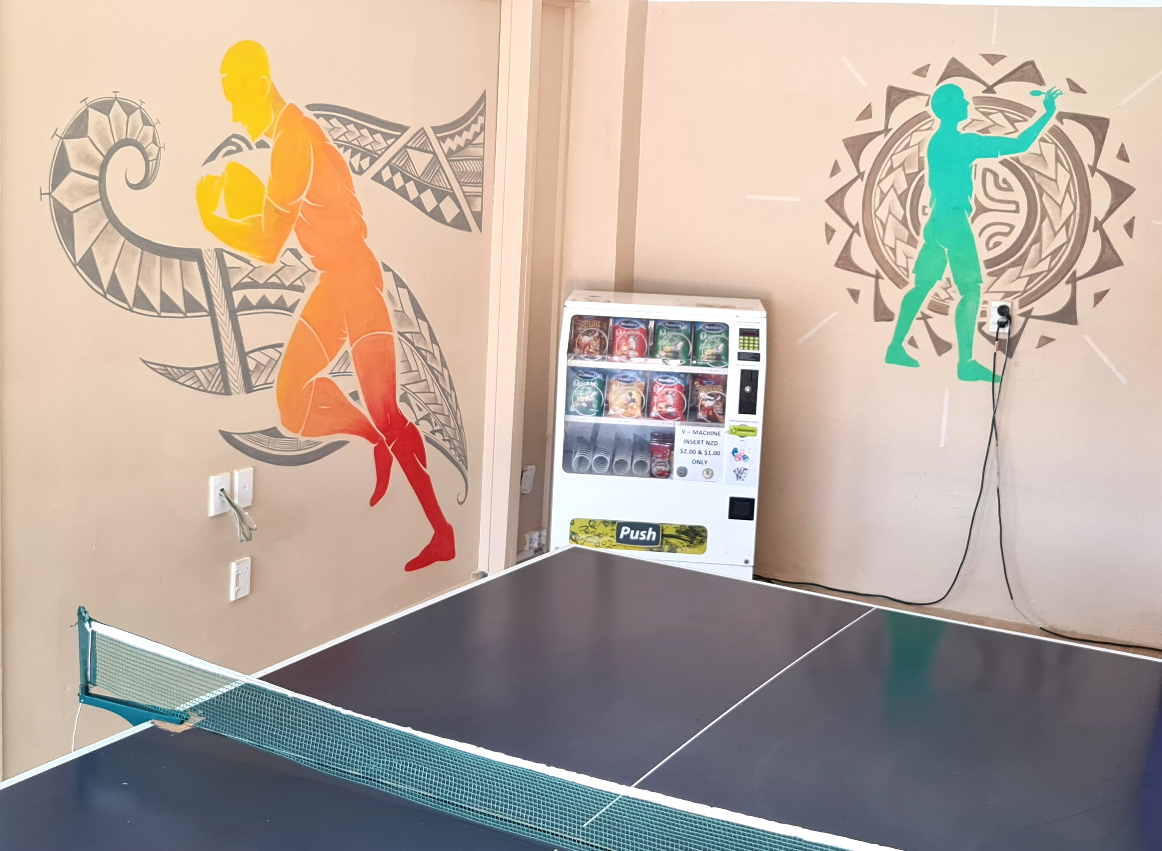 A ping pong table with a vending machine and two wall murals.