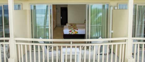 A balcony with a bed and a small table, a white railing, and a view of the interior.
