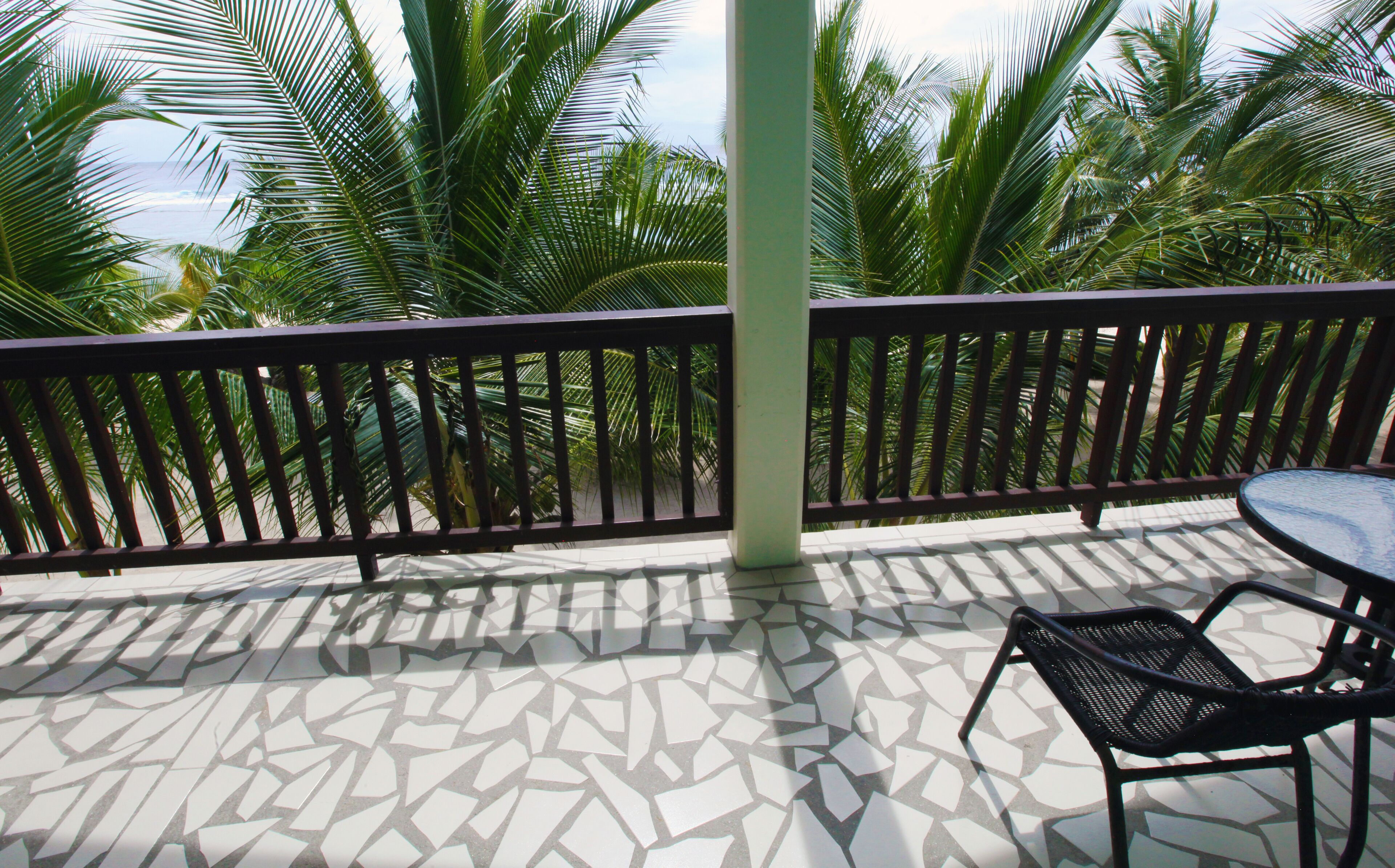 A balcony with a patterned floor, a metal railing, and a table with a chair.