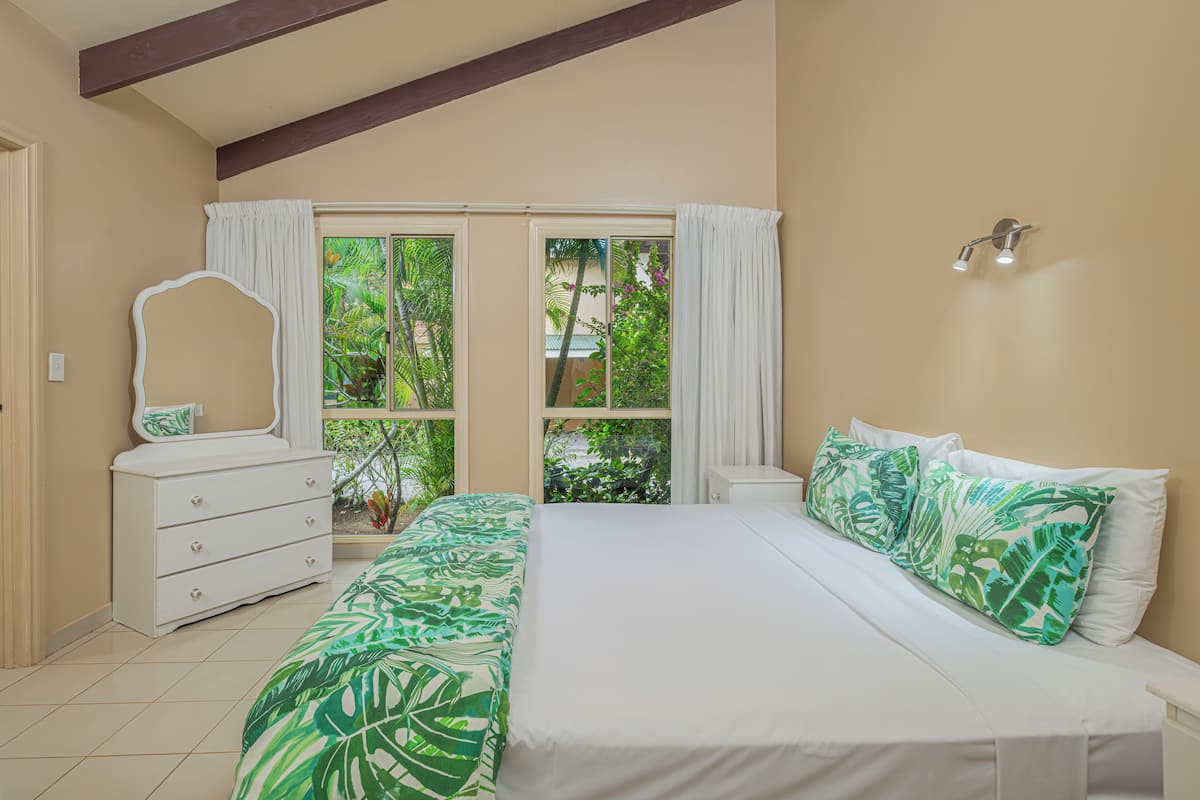 Une chambre à coucher avec un lit, une commode, un miroir et une fenêtre avec des rideaux.