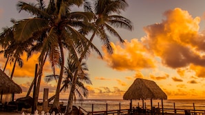 A beach scene with palm trees, a thatched-roof hut, and a chessboard. - The Edgewater Resort & Spa (Rarotonga)