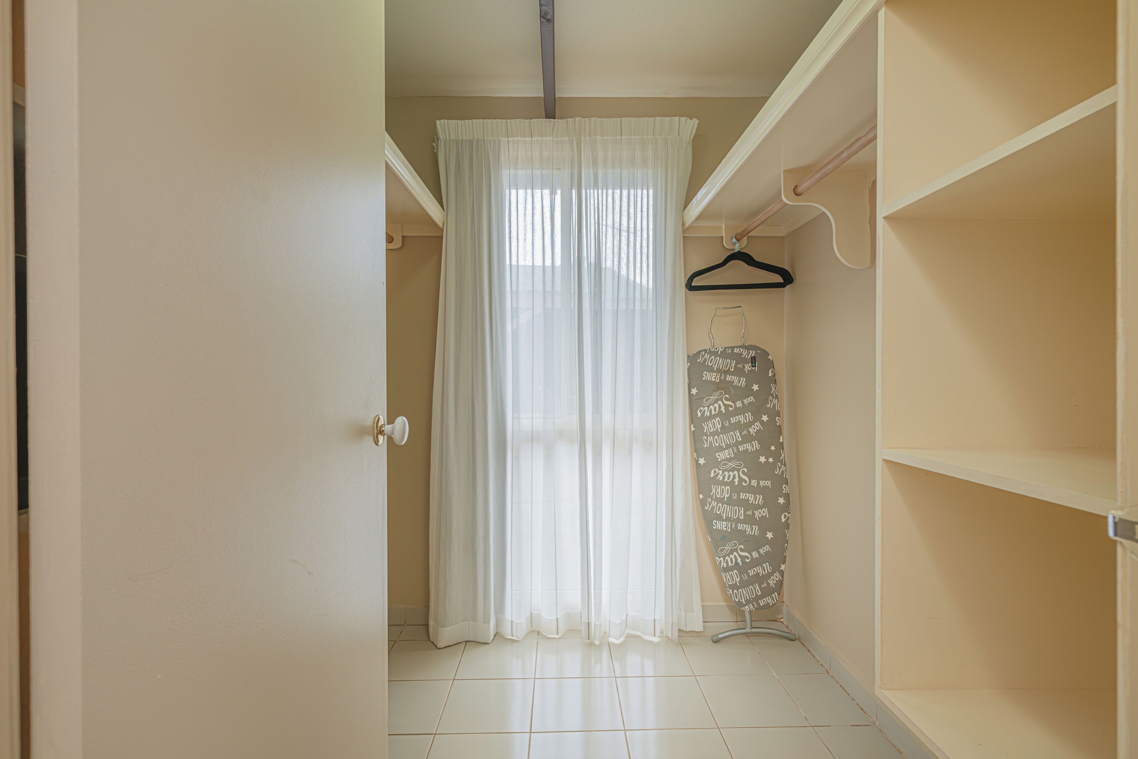 A room with a white door, a white curtain, a whiteboard with writing, and a white shelf.