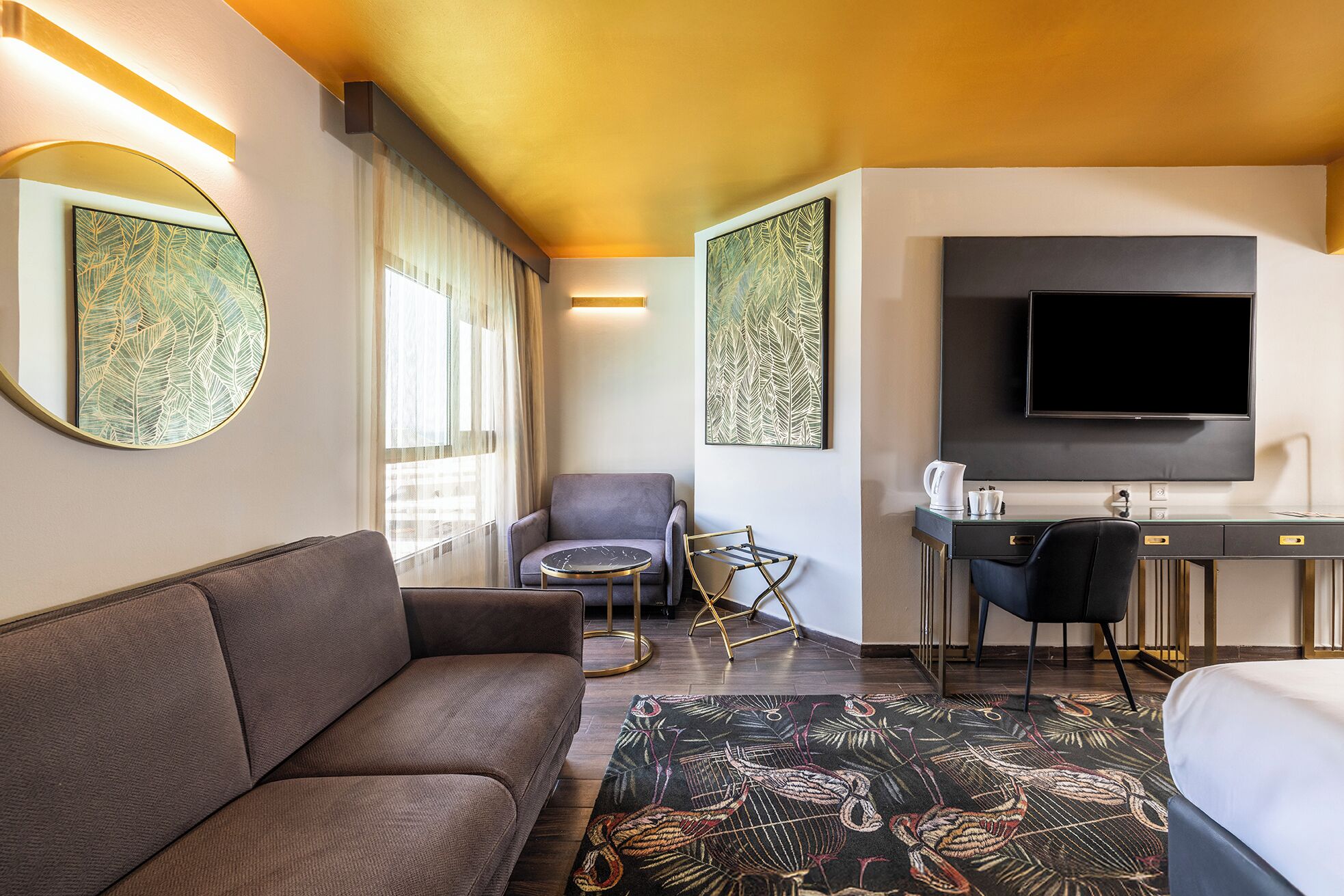 Habitación de hotel con sofá, escritorio, silla, televisor y obras de arte en las paredes.