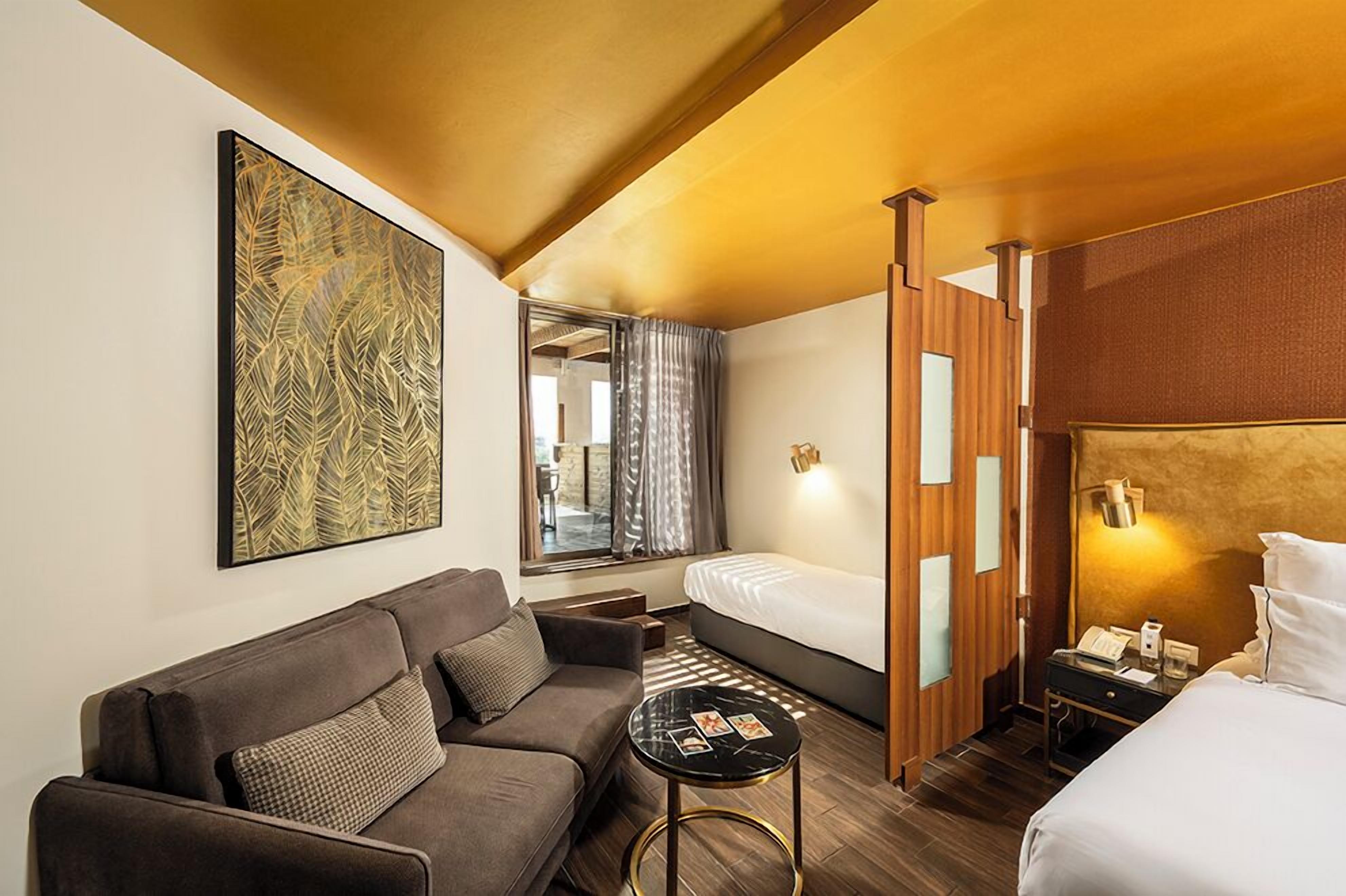 Une chambre d’hôtel avec un canapé, un lit, une petite table et une grande œuvre d’art accrochée au mur.