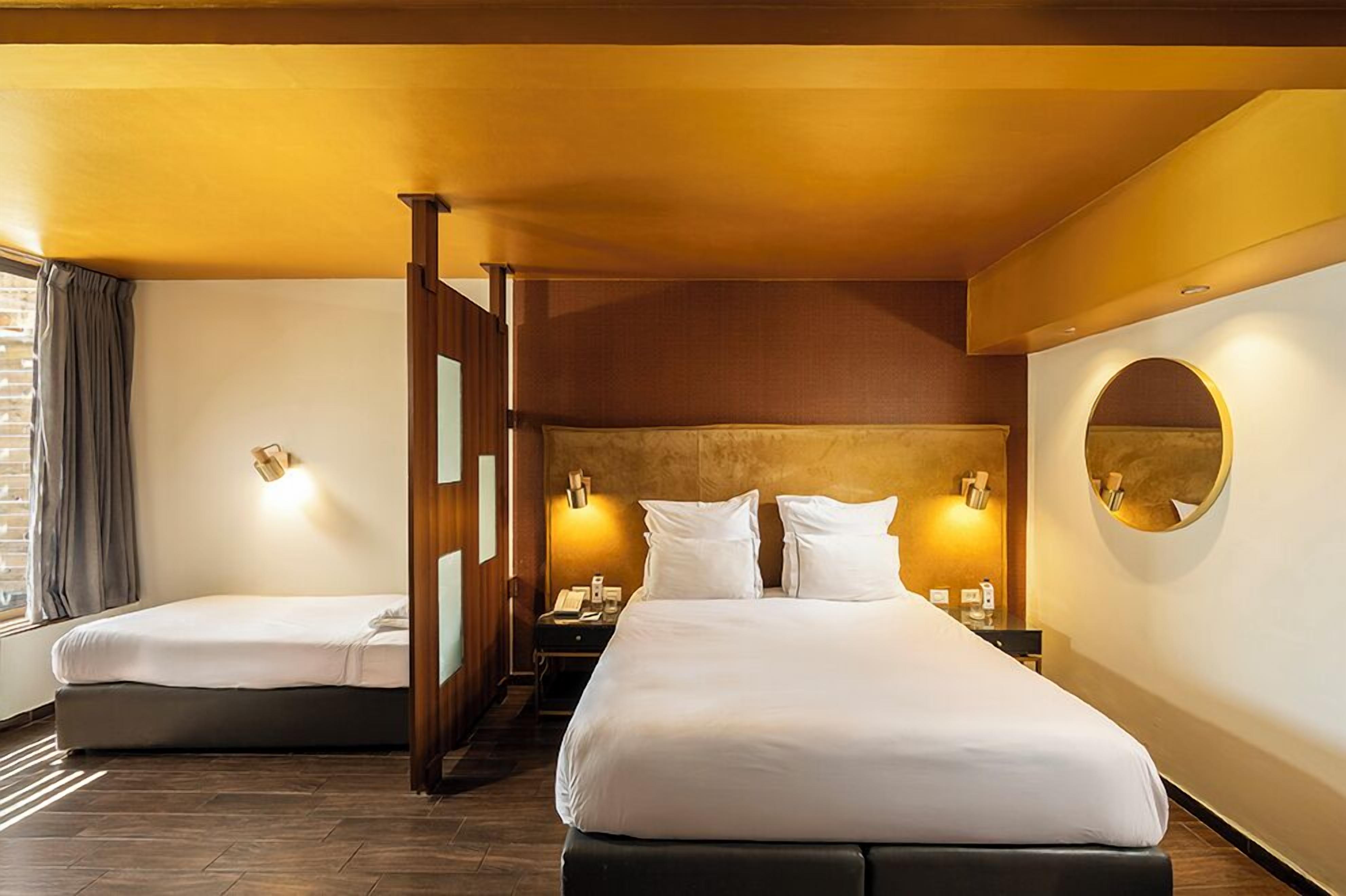 Ein Hotelzimmer mit zwei Betten, einem Holzkopfstück, einem runden Spiegel und Wandleuchten.