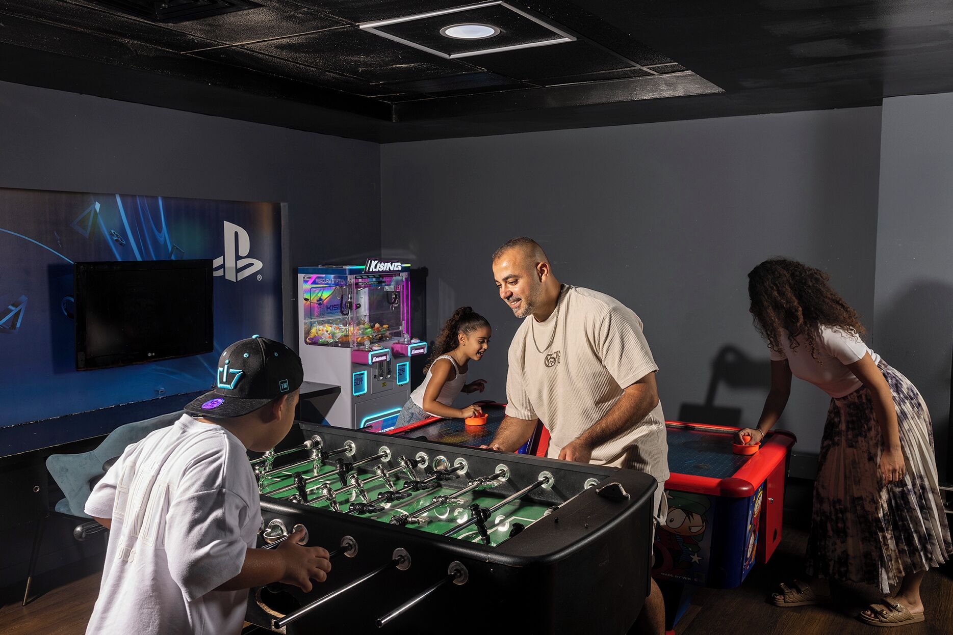 A room with a foosball table, a PlayStation display, and claw machines.