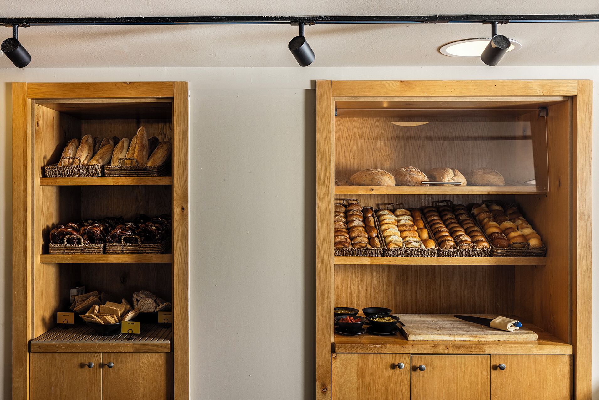 Two wooden display cases with shelves of bread and pastries, and a cutting board with a knife on the lower shelf.