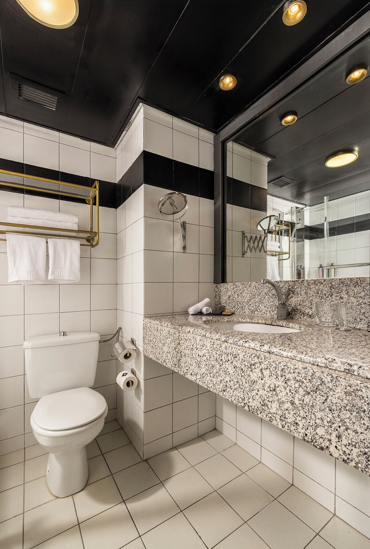A modern bathroom with a white toilet, a granite countertop sink, and a large mirror.