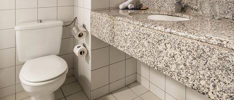 A modern bathroom with a white toilet, a granite countertop sink, and a large mirror.