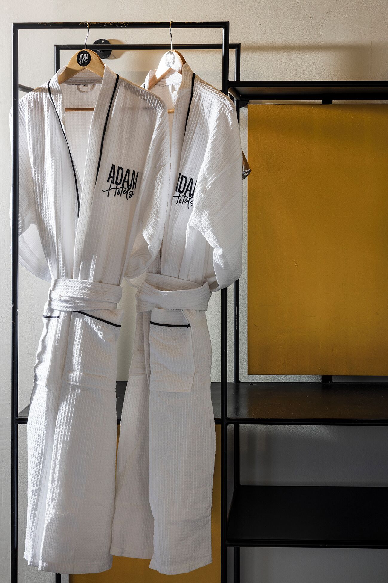 Two white robes with "ADAM Hotels" text hanging on a rack.