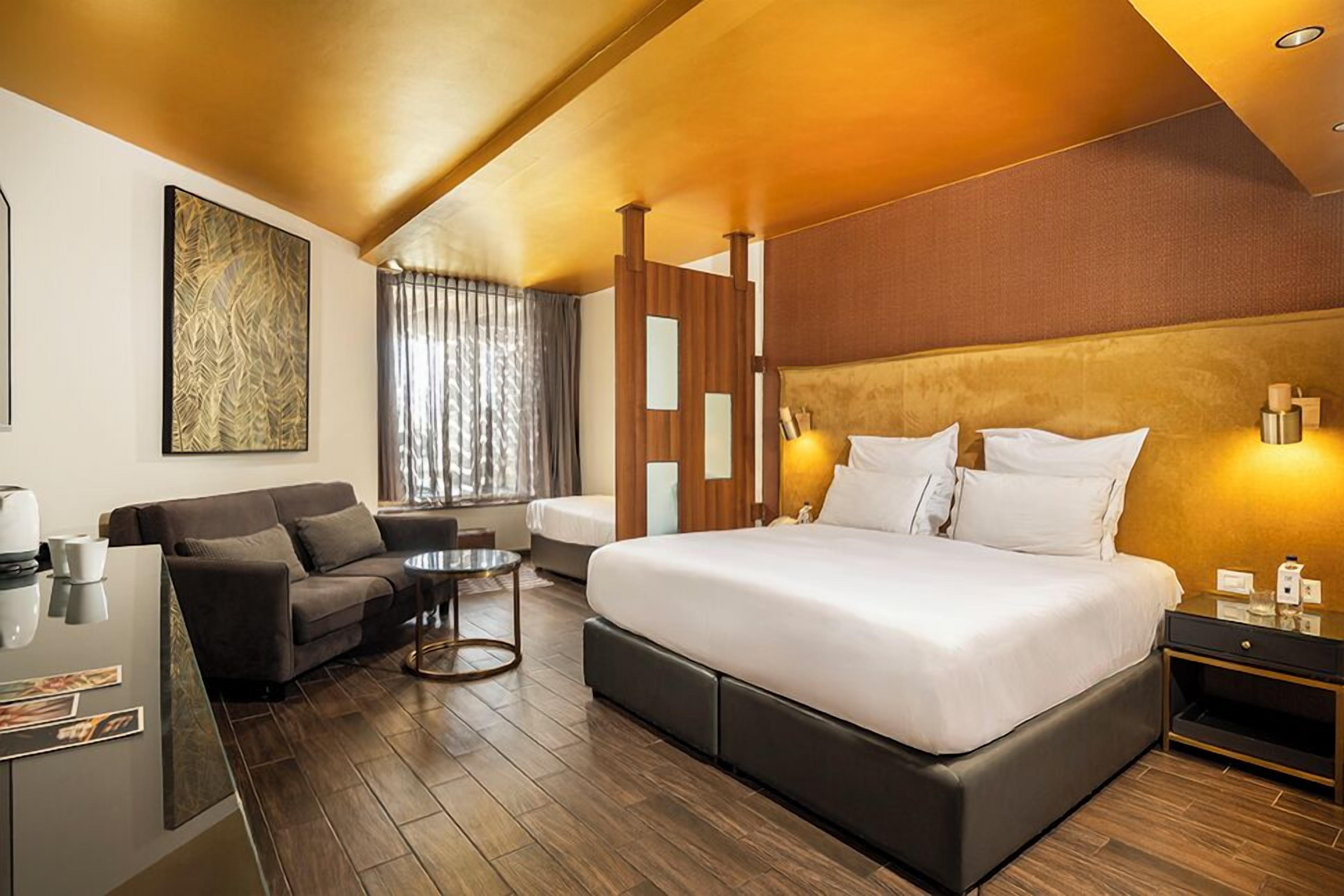 A modern hotel room with a large bed, a sofa, a small table, and a desk with a lamp.