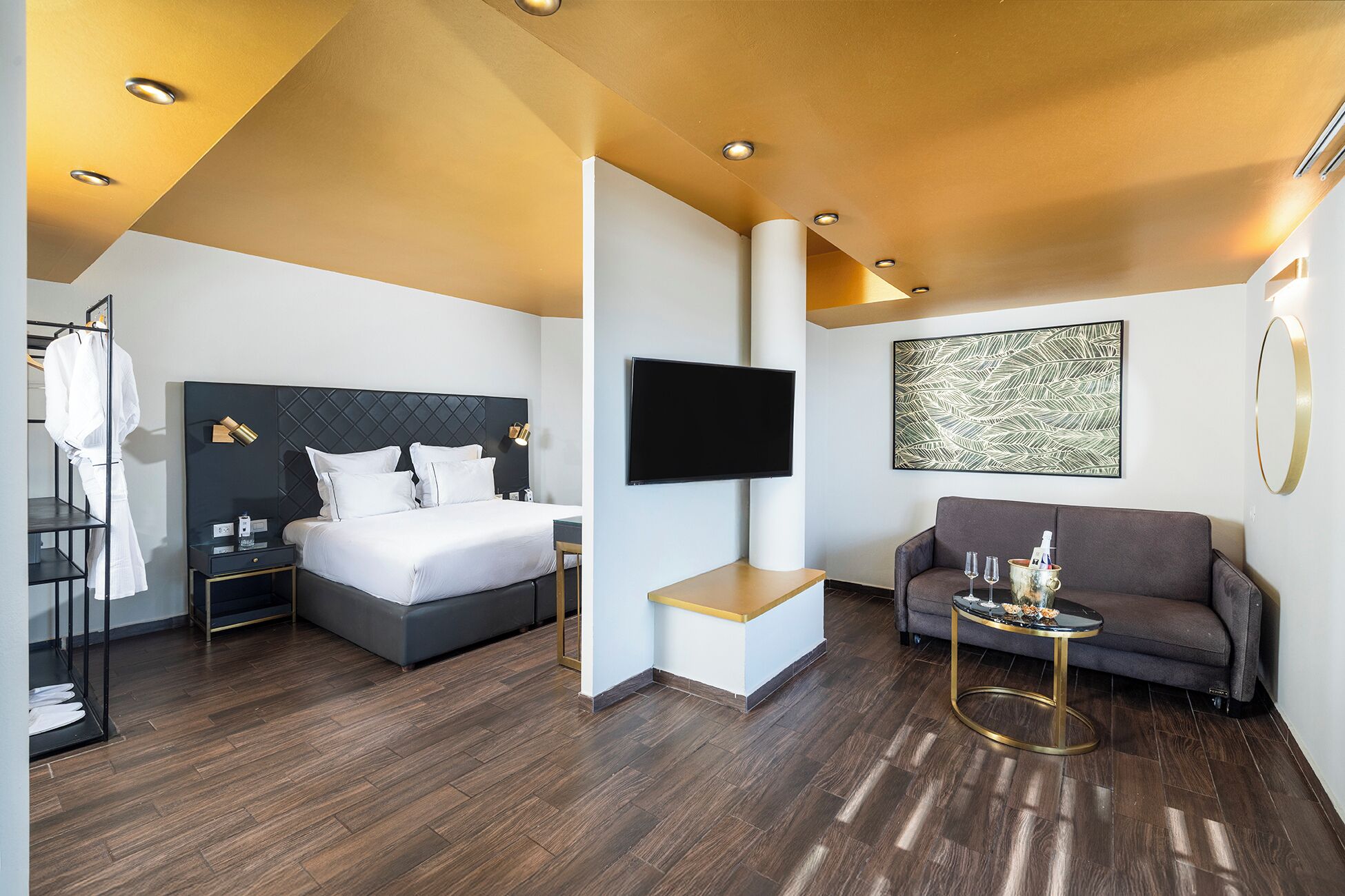A modern hotel room with a bed, a sofa, a TV, and a wooden floor.