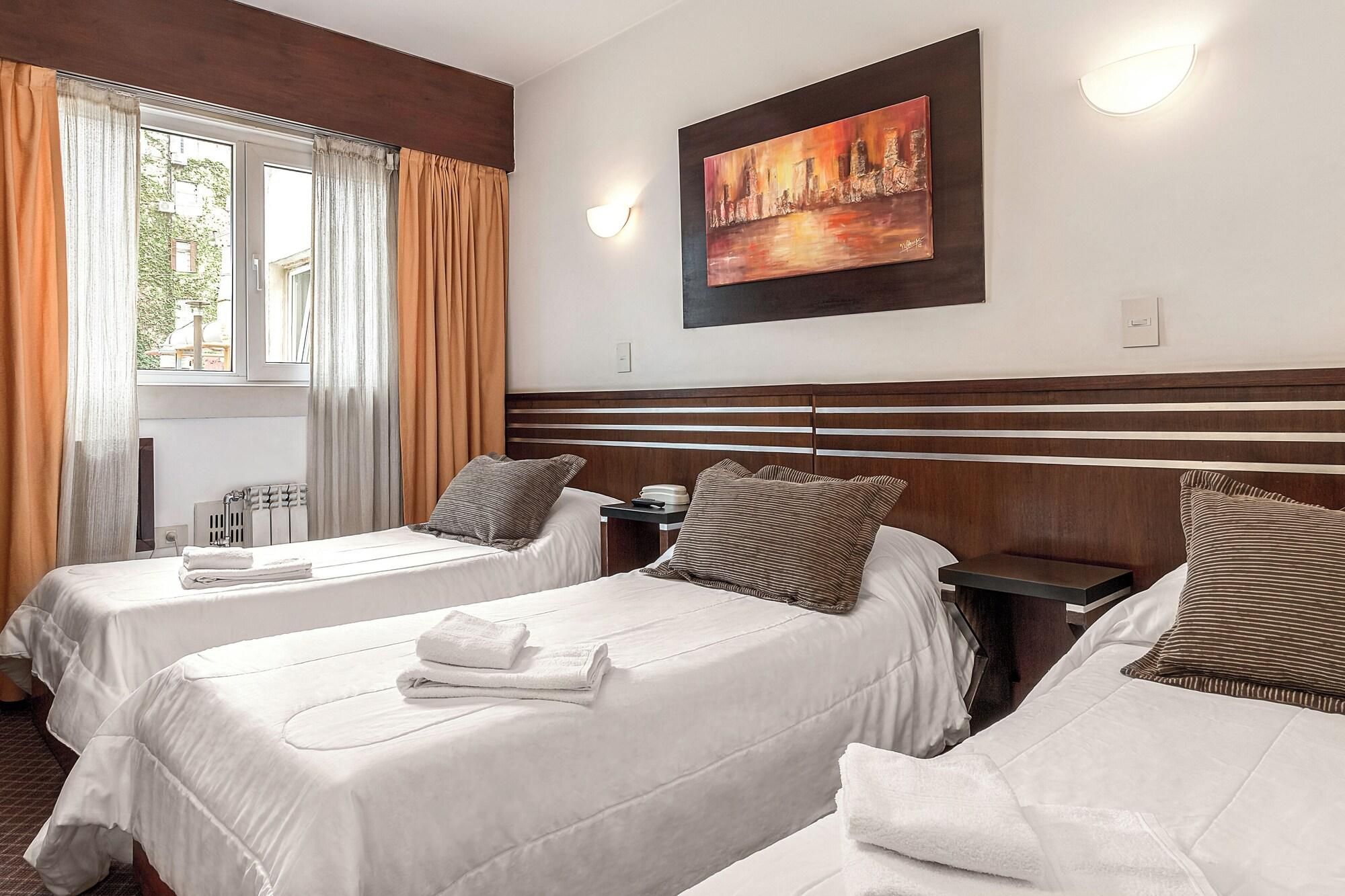 A hotel room with two beds, a painting on the wall, and a window with curtains.