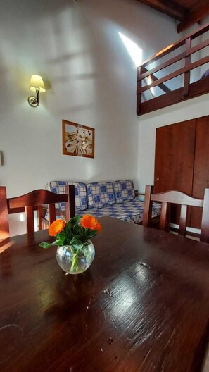 Una mesa de comedor con un jarrón de flores naranjas, un banco de madera y una lámpara fijada a la pared.