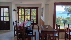 A dining area with a table and chairs, large windows with a view of the outdoors, and a door.