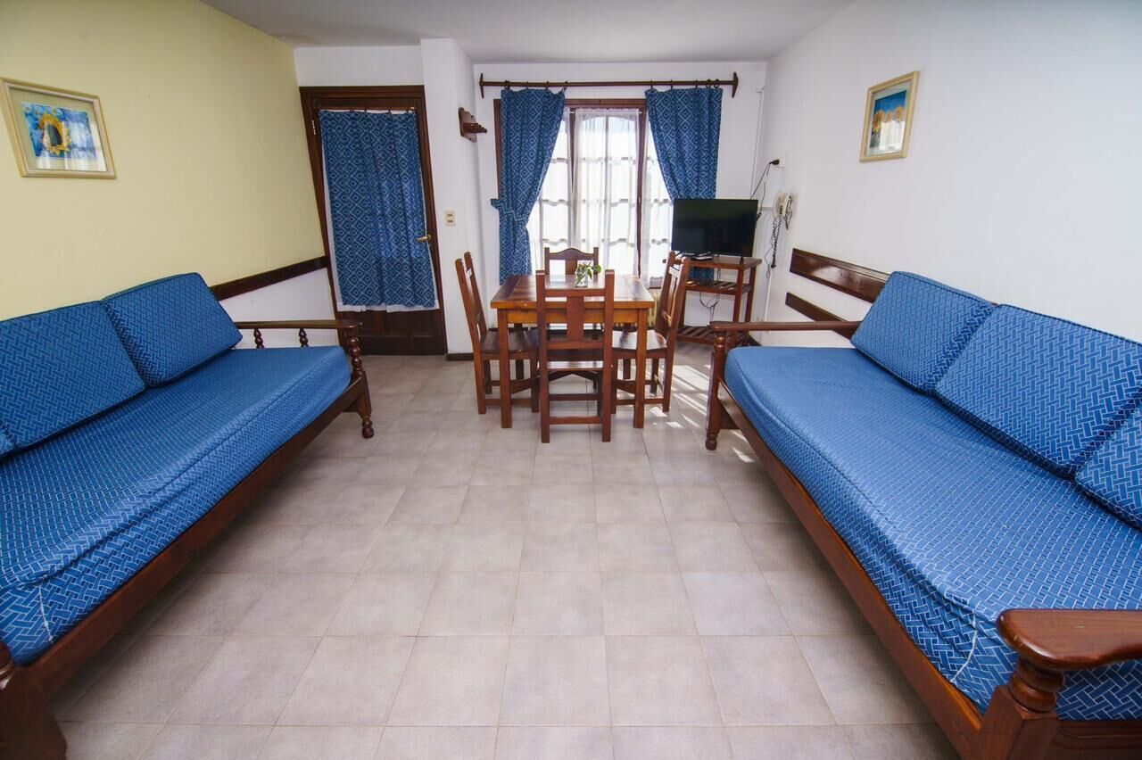 Una habitación con dos sofás azules, una mesa de comedor de madera, sillas, un televisor y cortinas.