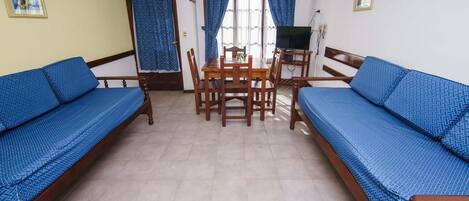 Una habitación con dos sofás azules, una mesa de comedor de madera, sillas, un televisor y cortinas.