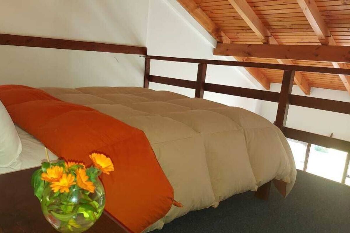 A bed with a wooden headboard, a vase with flowers, and a window in the background.