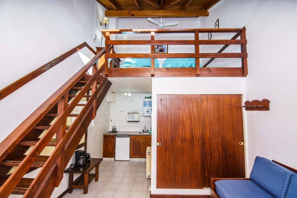 A loft-style room with a wooden staircase, a kitchen area, and a bunk bed.