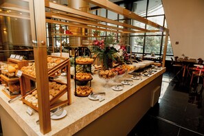 A buffet area with various baked goods and pastries displayed on wooden stands and glass bowls. - Royal Golden Savassi Hotel (Belo Horizonte)