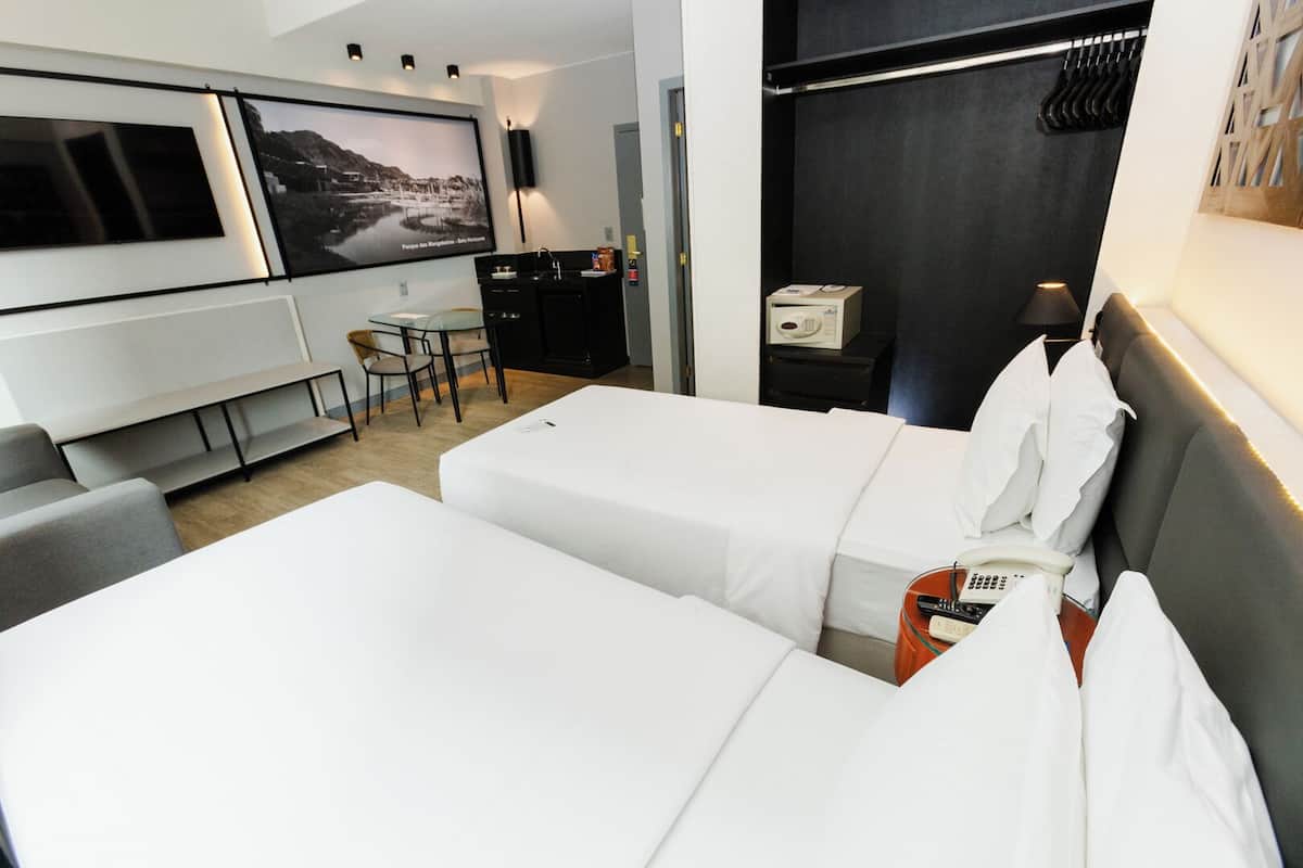 Une chambre d’hôtel avec deux lits, un bureau, une chaise, une télévision et une vue sur un paysage montagneux.