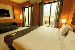 A hotel room with a large bed, a sofa, a TV, and a balcony with a view.