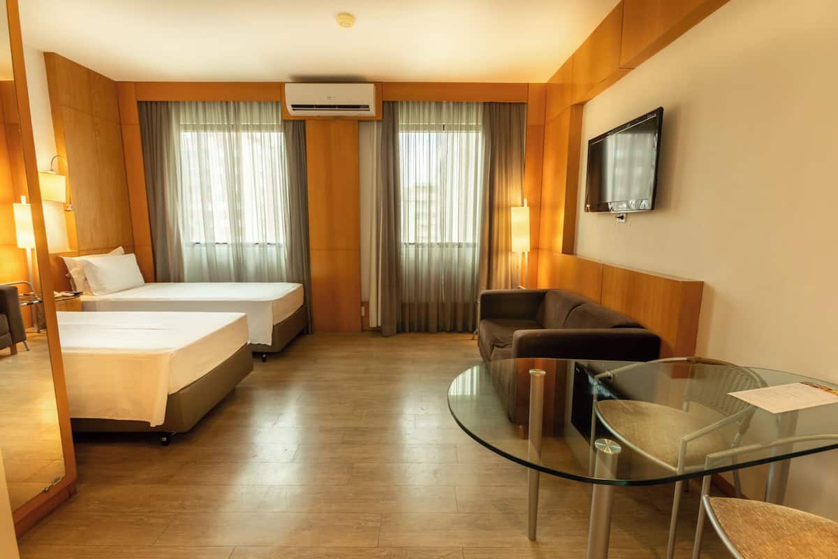 Une chambre d’hôtel avec deux lits, un canapé, une table en verre et un téléviseur fixé au mur.