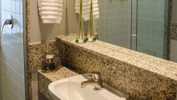 Casa de banho com bancada de granito, pia branca e duas toalhas penduradas num suporte de metal.