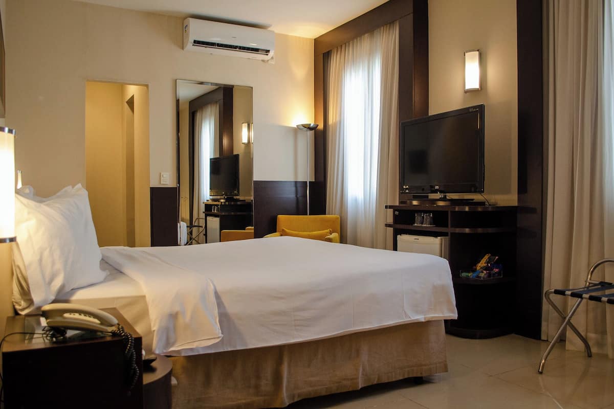 Ein Hotelzimmer mit einem Bett, einem Schreibtisch mit Telefon, einem Fernseher und einem Sessel.
