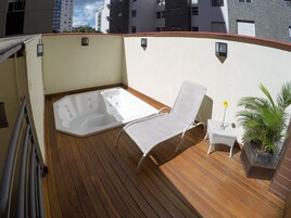 Una terraza en la azotea con una bañera de hidromasaje, sillas de descanso y una pequeña mesa con una planta en maceta.