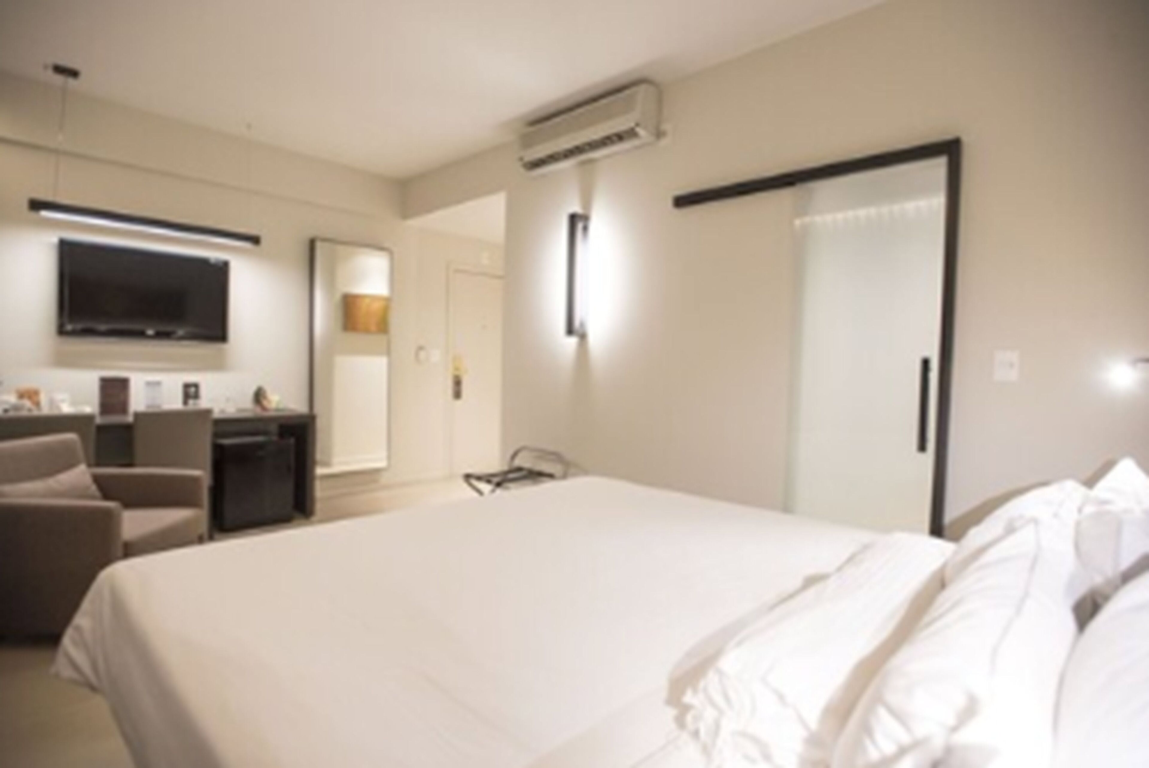 A hotel room with a large bed, a desk with a flat-screen TV, a chair, and a wardrobe.