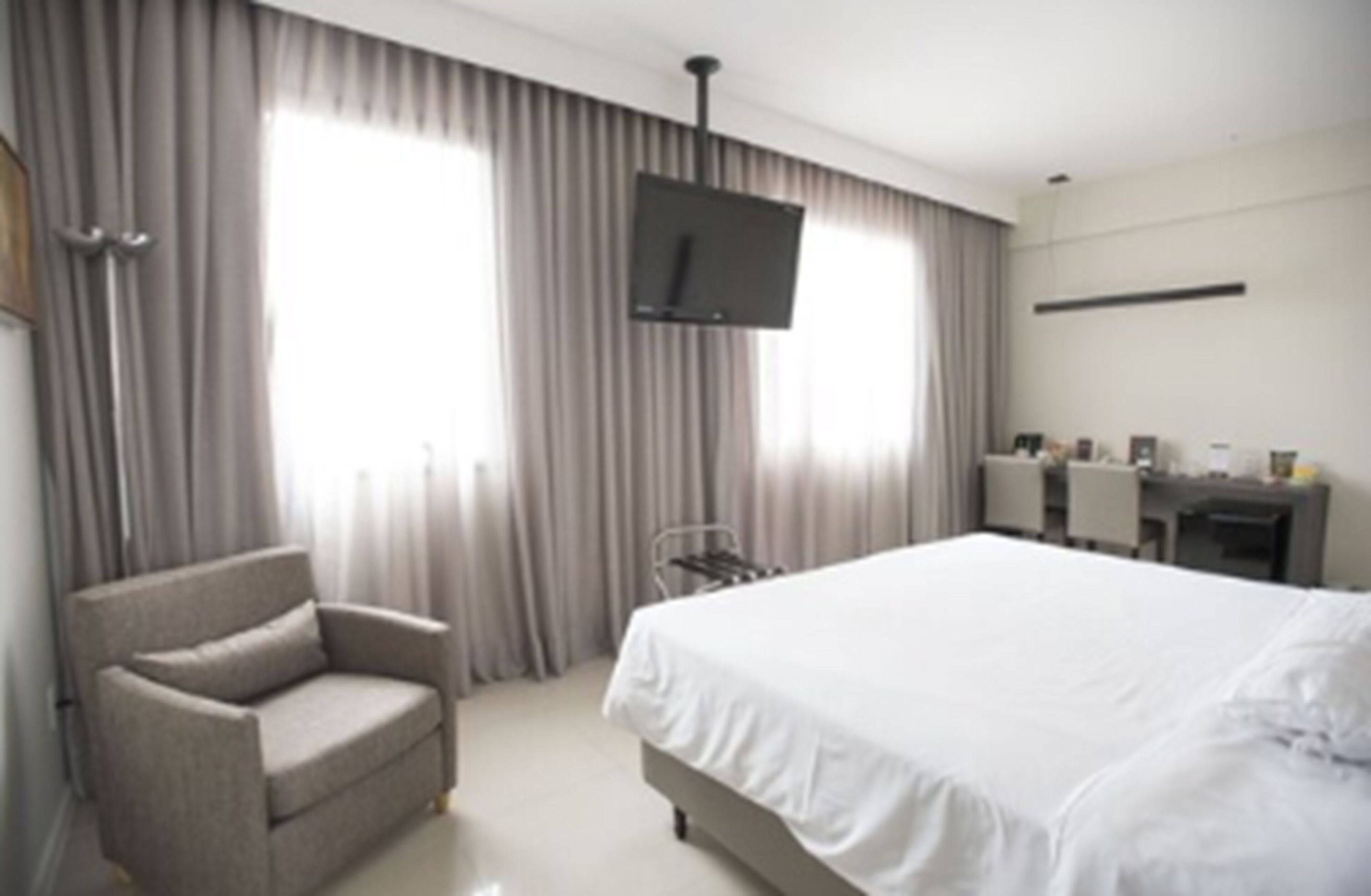 A hotel room with a bed, a chair, a desk, and a television.