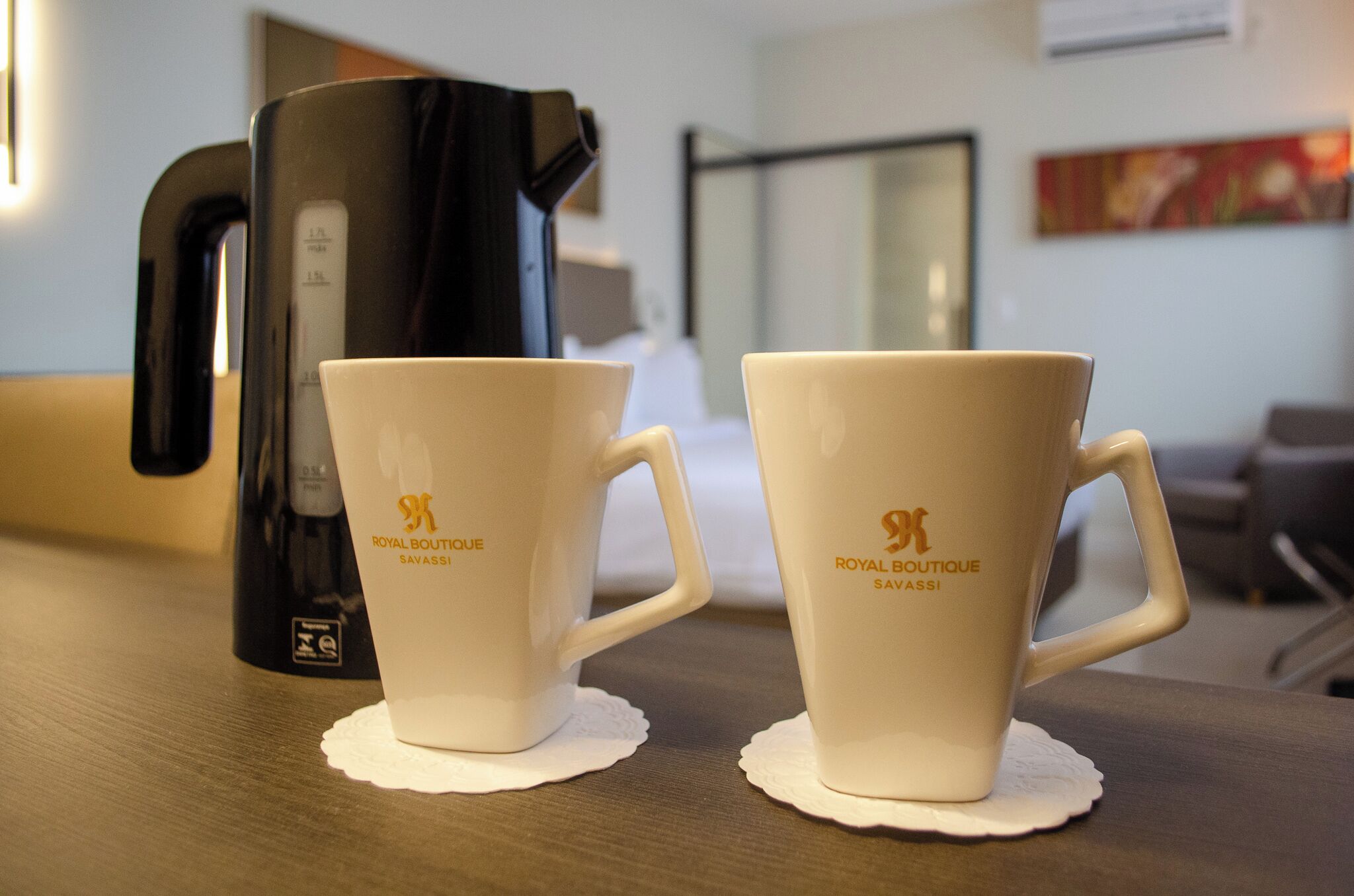 Zwei weiße Royal Boutique Savassi Tassen auf einem Holztisch, im Hintergrund ein schwarzer Kaffeeautomat.