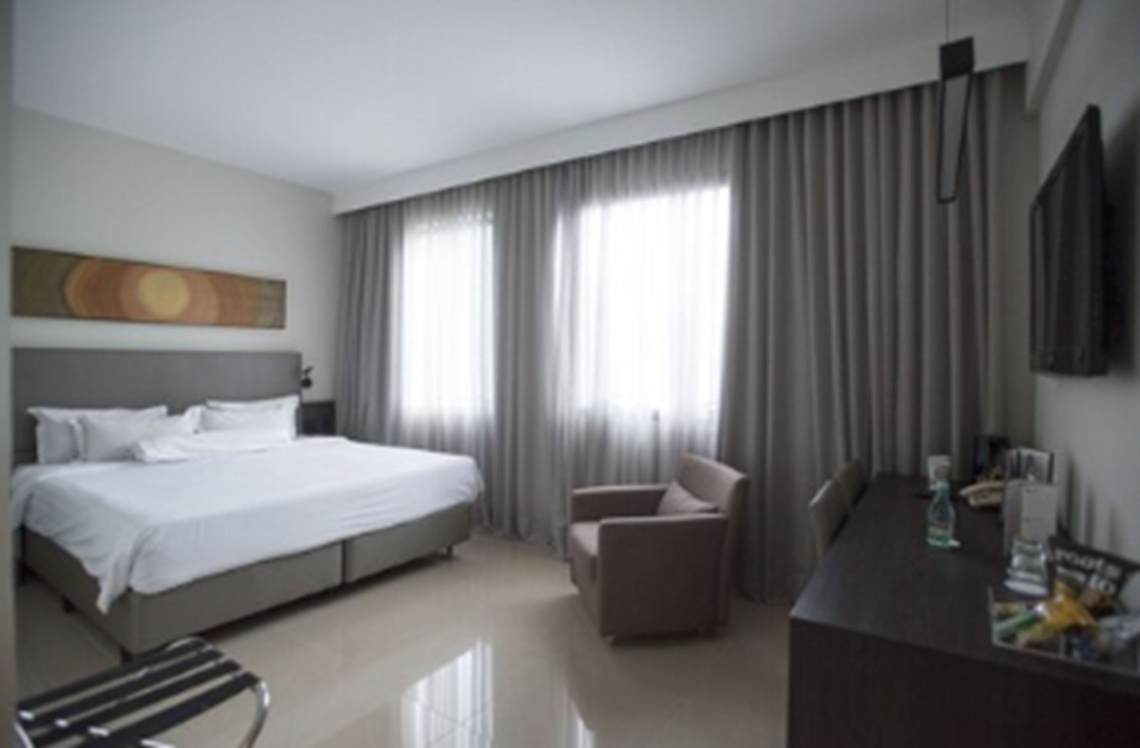 Habitación de hotel con una cama grande, un escritorio, una silla y un televisor en la pared.
