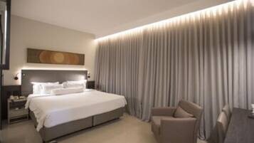 Una habitación de hotel moderna con una cama grande, una zona de estar y vistas a la ciudad a través de la ventana.