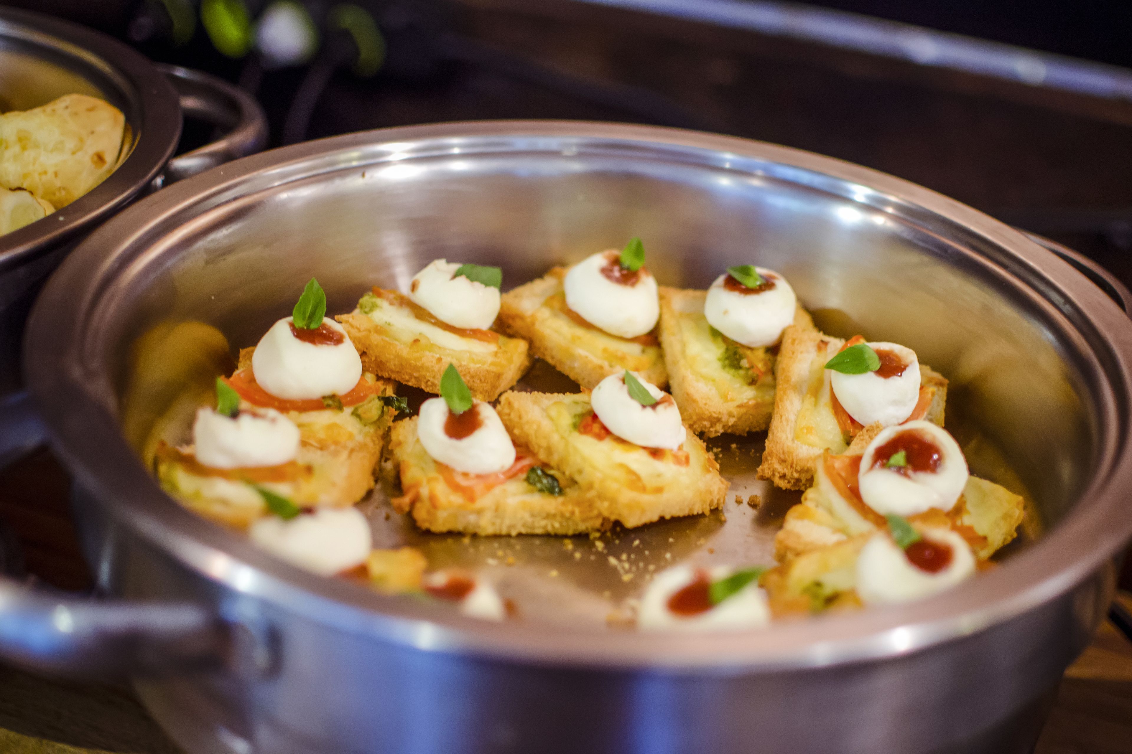 En skål av rostfritt stål som innehåller aptitretare med mozzarella och gröna garneringar.