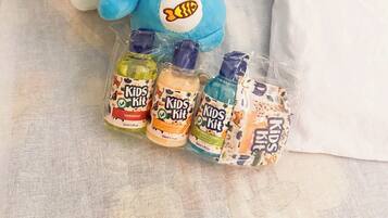 Un jouet en peluche et trois bouteilles de shampoing et d’après-shampoing pour enfants sont posés sur un lit.