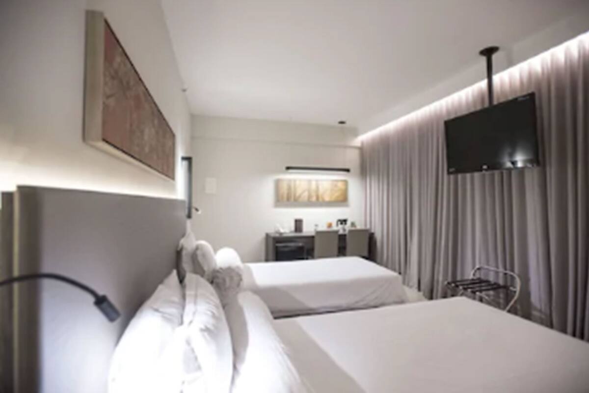 Ein Hotelzimmer mit zwei Betten, einem Schreibtisch, einem Fernseher und einem großen Fenster mit Vorhängen.