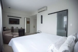 Habitación de hotel con una cama grande, un escritorio, una silla, un televisor y un espejo.