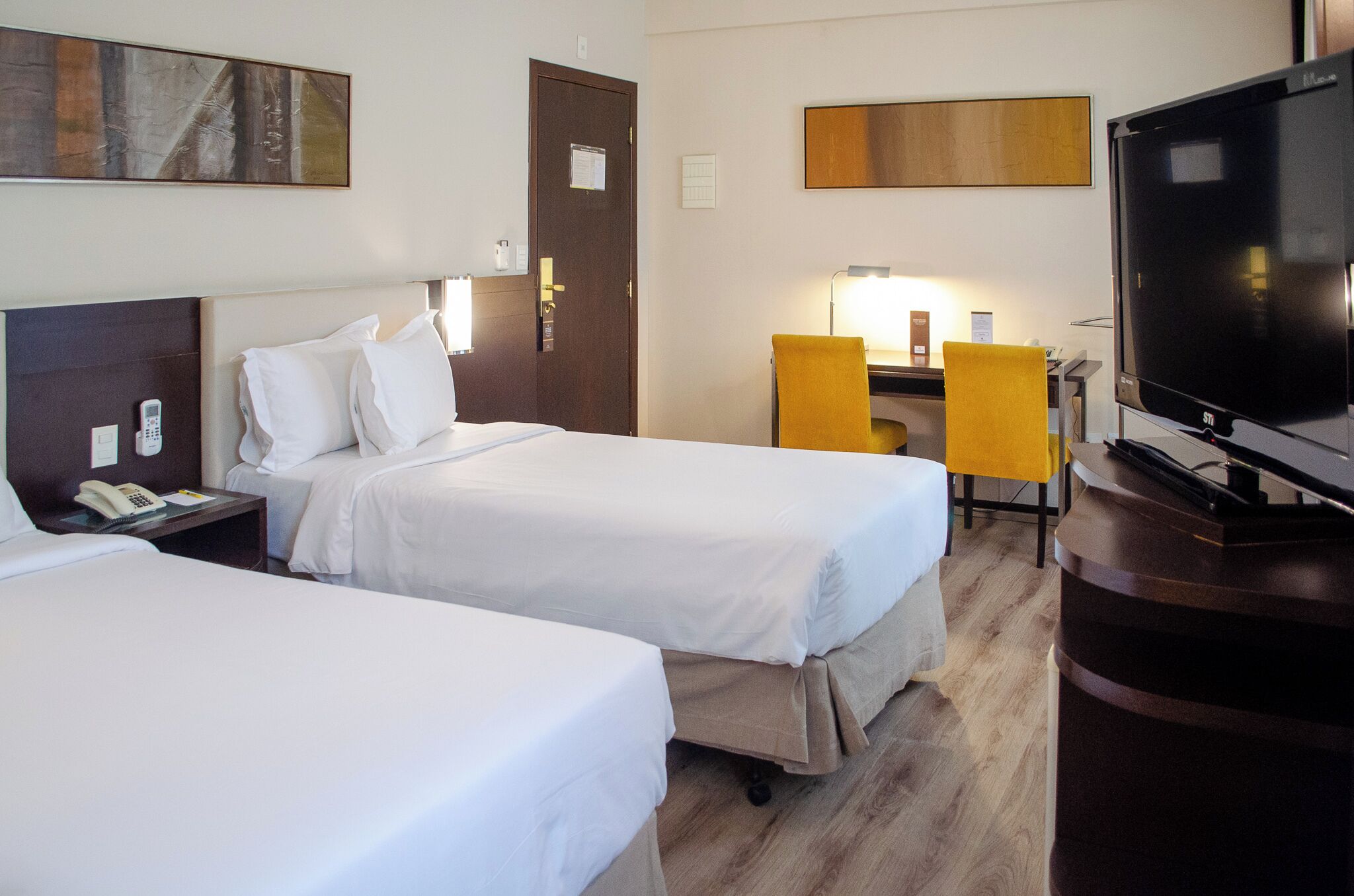 A hotel room with two beds, a desk with a chair, a TV, and a telephone.