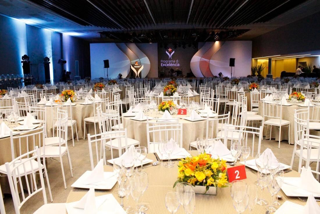 A banquet hall with round tables, white chairs, and floral centerpieces.